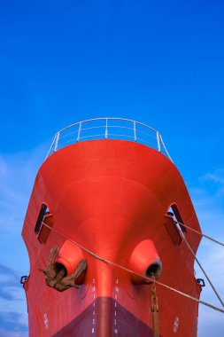 Dikey çerçevede mavi gökyüzü arkaplanına bağlama halatı ile limana demirlenmiş kırmızı petrol tankeri, kopyalama alanı ile alçak açı görünümü