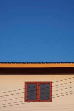 Sokak mimarisinin arka planı çok az. Dikey çerçeveli mavi gökyüzüne karşı elektrikli kablo hatları olan beyaz, ahşap bir evin tahta pencereleri.