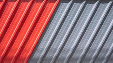 Çapraz desenli kırmızı ve gri kıvrımlı çelik çit arka planda güneş ışığı ve yüzeyde gölge var.