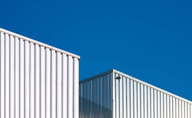 Two Corrugated Metal Industrial Warehouse Buildings against blue clear sky background in perspective side view