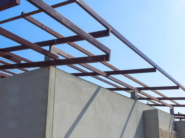 Metal shed roof framing structure on concrete house wall in construction site, low angle and perspective view