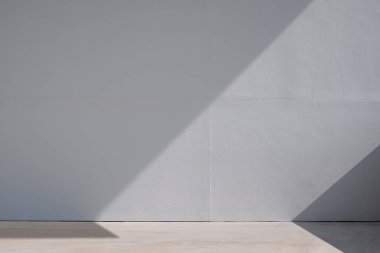 Light and shadow on surface of blank gray gypsum board wall and concrete floor, front view with copy space