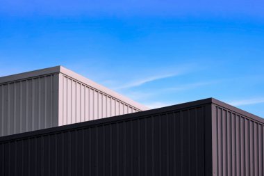 High section of 2 black and white corrugated metal Factory Buildings against blue sky background