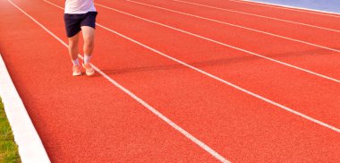 Low section of young man jogging on running track in outdoors stadium, panoramic view with motion blurred