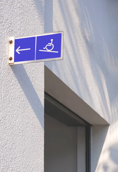The old Disabled Wheelchair Sign and arrow label on white wall of building entrance way for people with disabilities, side view and vertical frame