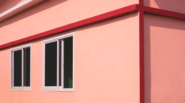 Sunlight and shadow on surface of glass sliding windows on orange concrete wall with red edge of modern house in perspective side view