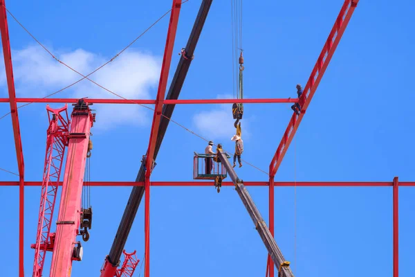 Construction workers with Crane truck are installing Sling Wire Ropes to secure metal Roof Structure of Factory Building in construction Site against blue sky background