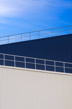 Modern beyaz ve siyah kıvrımlı metal duvar fabrika binalarının çatısında çitle çevrili dikey çerçeveli mavi gökyüzü arkaplanı