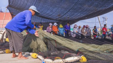 Samut Sakhon, Tayland - 31 Mart 2023: Asyalı Balıkçı ve işçi grubu açık verandadaki kırık ağları onarıyor