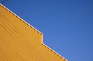 Yüzeyinde elektrik kablolarının gölgesi olan renkli sarı bina duvarının sokak minimal mimari biçimi mavi açık arkaplana karşı