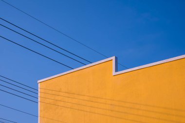 Eski Vintage sarı bina duvarının sokak minimal mimari stili. Mavi berrak gökyüzü arkaplanına karşı elektrik kabloları, perspektif düşük açı manzaralı.