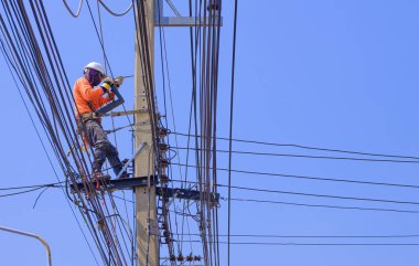 Elektrikçi mavi berrak gökyüzü arka planına karşı elektrik direğine elektrik sistemi kurmaya çalışıyor