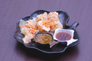 Buğulanmış domuz eti ve karides köftesi, deniz ürünleri ve dekoratif siyah seramik tabakta özgün soslar, klasik tarzda.