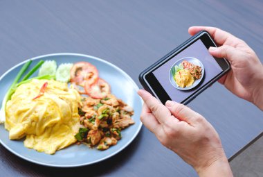 Kadın eli, ahşap masada Asya sokak yemeğinin fotoğrafını çekmek için akıllı telefon kullanıyor.