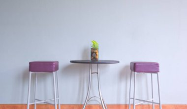 Şeytanın sarmaşık bitkisi cam vazoda yuvarlak masada, içi boş gri iç duvarın yanında 2 deri sandalye, ön manzara ve fotokopi alanı