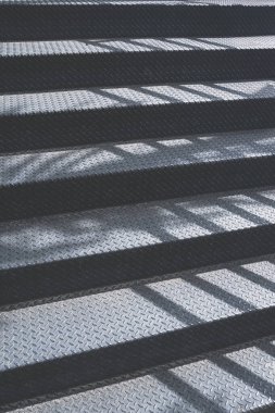 Doğanın kara metal merdivenlerinin yüzeyindeki güneş ışığı ve gölgesi halka açık parkta dikey çerçevede yürür.