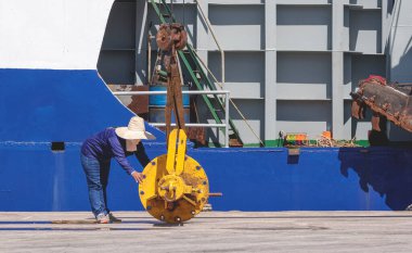 Asyalı kadın işçi, vinçli sarı hidrolik silindiri limandaki kum emici gemisine aktarmaya çalışıyor.