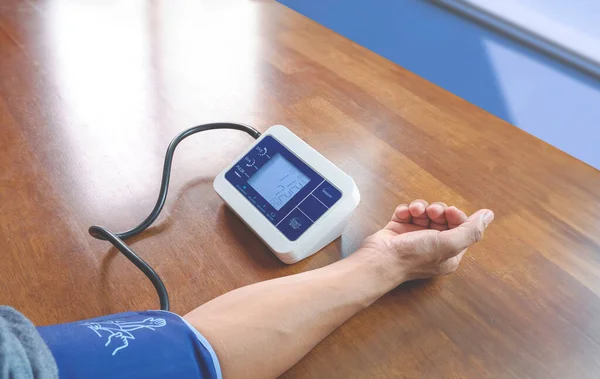 自宅の木のテーブルで血圧を測定するためにデジタルスパイグマノメーター機械を使用する男の手 ヘルスケアの概念 — ストック写真