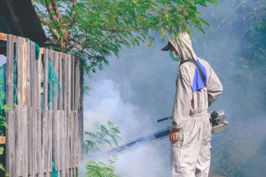 Sivrisinekleri yok etmek ve eski evin dışındaki aşırı gelişmiş bölgelerde Dang hummasını önlemek için sis püskürtme makinesi kullanan sağlık çalışanı.