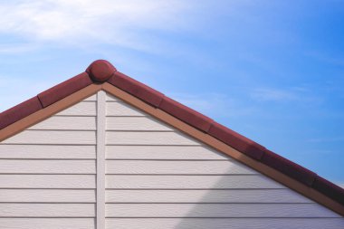 Mavi gökyüzü arkaplanına karşı klasik evin beton kahverengi çatı fayansı olan beyaz yapay ahşap bir çatı.