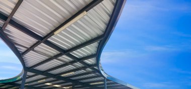 Mavi gökyüzü arka planına karşı siyah çelik kiriş yapısı, aşağıdan görünümü ve panoramik manzarası olan modern eğimli metal eğri çatılı yürüyüş yolu.