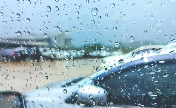 Rain drops on car glass window surface of driver\'s door while parked in outdoors parking lot during rainy weather