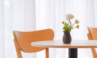 Modern kahve dükkanının beyaz perdesinin önündeki ahşap sehpanın üzerindeki siyah seramik vazodaki beyaz suni çiçeklere odaklan.