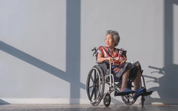 Asian mental healthy elderly woman on wheelchair relaxing in resting area while waiting for her annual medical checkup inside of hospital. Health care and good mental health concept