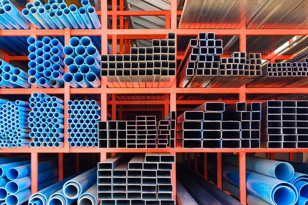 Various sizes of many carbon steel rectangular and square tubes with blue PVC water pipes on storage shelf of building supply store