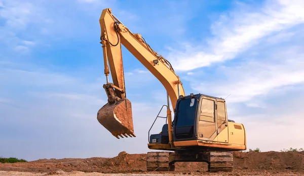 Yellow excavator is leveling the ground for construction area of industrial building in construction site against blue sky background