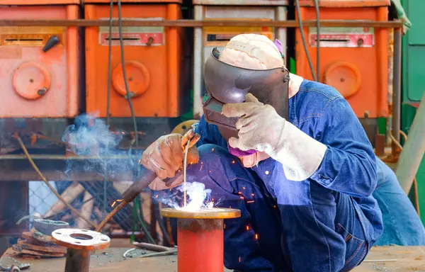 Kaynakçı, petrol boru hattının geliştirilmesi için çelik boruya bağlanmak üzere metal kaplama yapıyor.