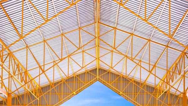 Yellow metal roof beams and aluminum corrugated tile roof of industrial building with blue sky background, symmetric and inside view