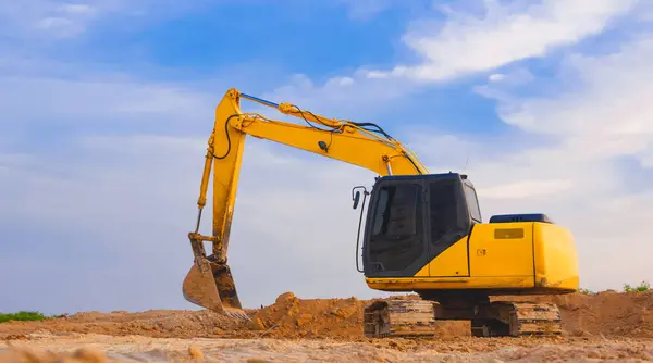 Yellow excavator is leveling the ground for construction area of industrial building in construction site against blue sky background