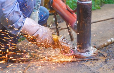 Kaynakçı el, petrol boru hattının çalışmasını geliştirmek için çelik borulardaki metal flanşları cilalamak için elektrikli öğütücü makinesi kullanıyor.