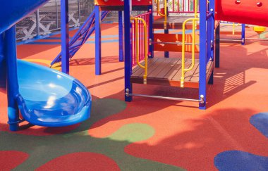 Çocuk parkındaki çocuk parkındaki renkli lastik zeminde mavi slaytlı tırmanma ekipmanları.