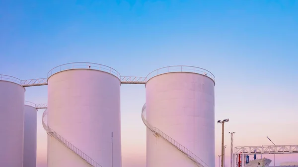 Group of white Storage Fuel Tanks with oil pipeline system in Petroleum Industrial area at harbor against dusk sky background