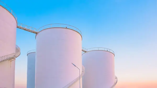 Group of white storage fuel tanks in petrochemical industrial area against beautiful dusk sky background, low angle view with copy space
