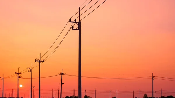 stock image Silhouette row of electric power poles with cable lines against orange sunset sky background