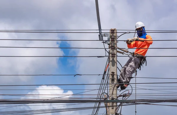 Güvenlik ekipmanı ve çeşitli iş araçlarına sahip elektrikçi. Elektrik direğine kablo hatları ve elektrik sistemi kurarak bulutlu gökyüzü arka planına karşı