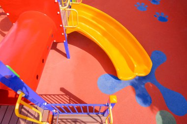 Açık hava oyun parkı ekipmanlarıyla dolu renkli bir kaydırak ve tünel anaokulunda kauçuk zemin üzerinde güneş ışığı ve yüzeyinde gölge, yüksek açı manzaralı.