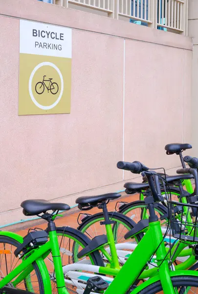 Row of green bikes parked in bicycle parking area outside of building with parking sign label on stone beige wall in vertical frame