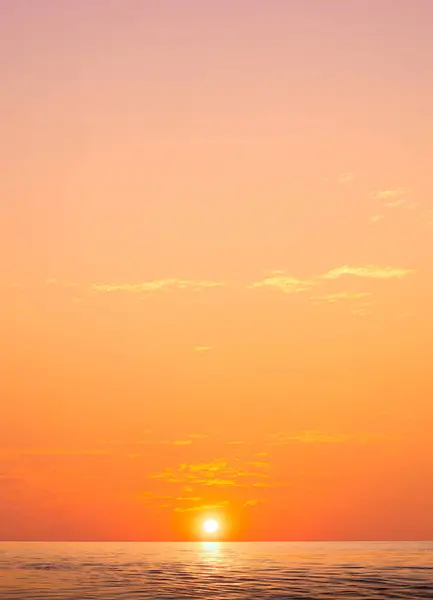 Golden sunrise sky vertical background over sea with yellow sunlight cloud on idyllic orange morning sky and light reflection on water surface, beautiful nature tranquil seascape in minimal style