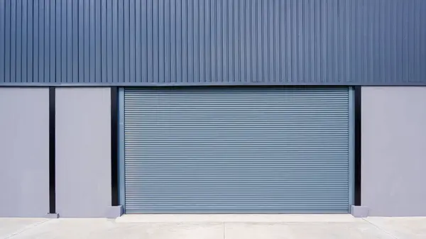Automatic roller shutter entrance door on gray concrete and corrugated metal wall of new modern warehouse building, front view with copy space