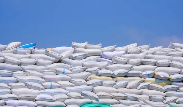 Many sacks of crushed plastic bottles or bottle flakes stacked on industrial yard area against blue sky background, recycling used plastic material to new synthetic fiber concept
