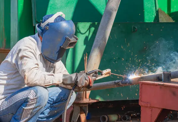 Welder with safety equipment using arc welding machine to welding galvanized steel pipe at workshop