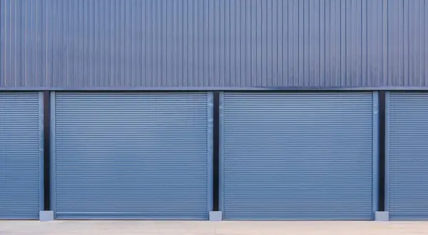 Automatic roller shutter entrance doors with corrugated metal wall of large gray warehouse building, front view with copy space