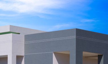 Modern ve minimal tarzda geometrik gri ve beyaz ofis binalarının pürüzlü beton duvarı mavi gökyüzü arka planına karşı
