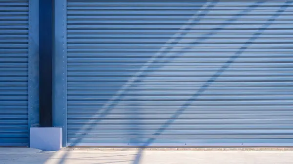 Beton zemin yüzeyinde ışık ve gölge olan büyük endüstriyel depo binasının otomatik gri perdeli giriş kapıları.