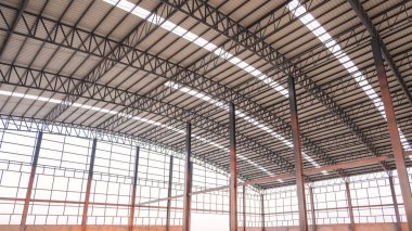 İnşaat alanındaki büyük endüstriyel fabrika binasının içinde metal kolonları ve eğri çatı kirişleri olan çelik duvar iskeleti yapısı, düşük açı ve yan bakış açısı