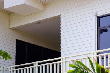 Koridor, iki katlı beyaz ahşap bir evin balkonuna, alçak açılı ve perspektiften bakan bir eve bağlanıyor.